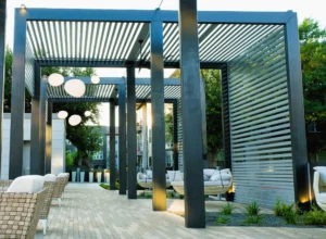 Black pergolas with horizontal slats over cushioned woven seating and hanging spherical lights in landscaped communal area