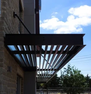 Metal canopy with parallel slats mounted above window, supported by rods on modern building facade
