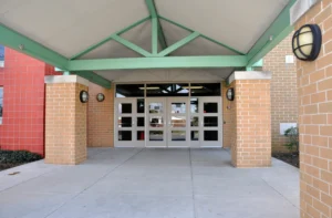 Triangular steel canopy with green beams and brick columns over school entrance